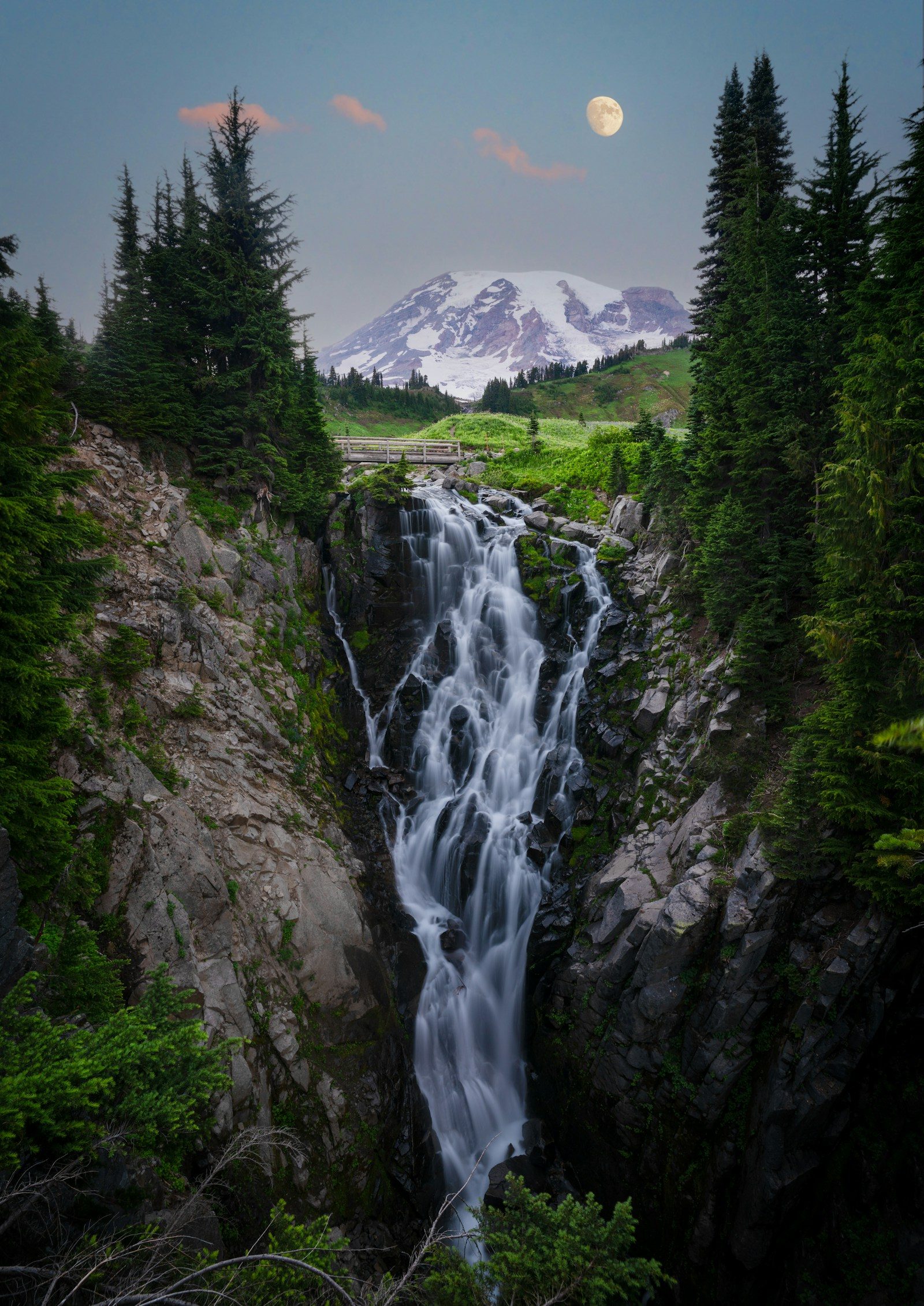 A waterfall below Mount Rainier at dusk with the moon rising